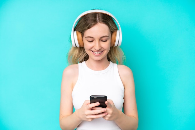 青色の背景に分離された金髪の英語の若い女の子音楽を聴いて、携帯電話を探しています