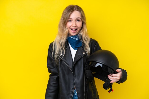 Blonde english young girl with a motorcycle helmet isolated on yellow background with surprise facial expression