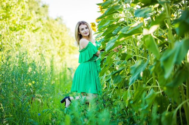 Blonde Europese vrouw in een groene jurk op aard met zonnebloemen