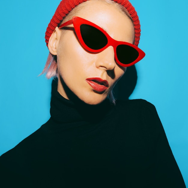 Блондинка в модной одежде и модных аксессуарах. Красная шапка и солнцезащитные очки в стиле ретро.