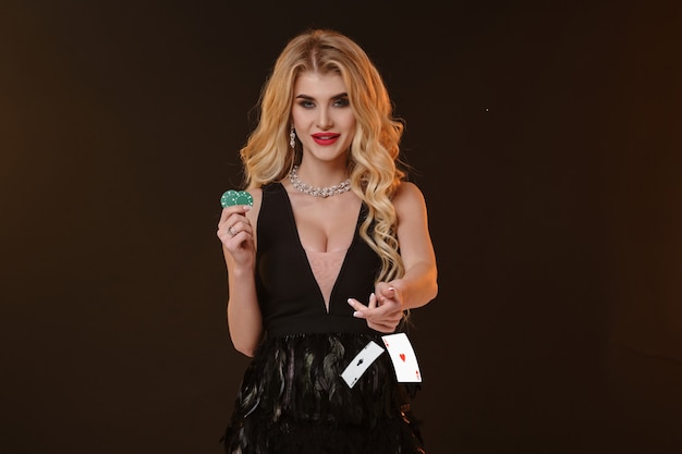 Blonde female in black dress and necklace smiling showing two green chips throwing something