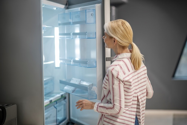Фото Блондинка покупательница выбирает холодильник в мегамагазине