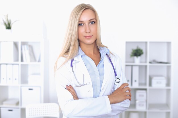 Blonde female doctor sitting at the table in  hospital and looking at camera.