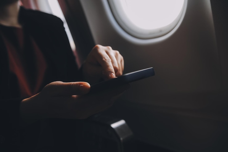 Photo ネットブックで飛行機の座席に座って ⁇ スマートフォンで受信通知をチェックしている金 ⁇ の女性観光客 ⁇ 飛行機の飛行中に携帯コンピュータで電話からメディアを共有する若いビジネスウーマン ⁇ 