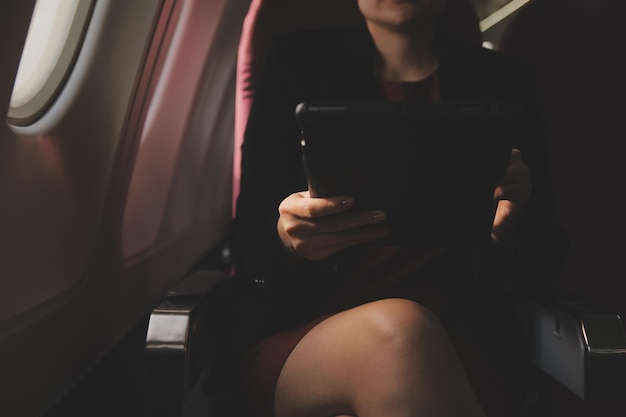 Blonde female tourist checking incoming notification on smartphone sitting on seat of airplane with netbookYoung businesswoman share media from telephone on laptop computer during plane flight