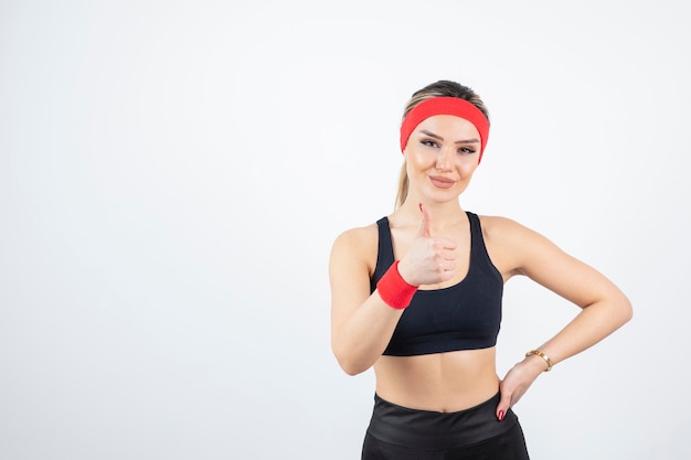 Blonde fit woman in black sportswear standing and showing thumb up.  