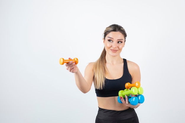 Blonde fit woman in black top standing and holding colorful dumbbells.  