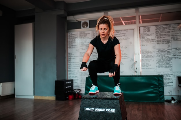 Blonde fit woman jumping on block in gym.