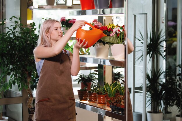 Foto donna bionda fiorista innaffia, si prende cura delle piante nell'area di lavoro di un negozio di fiori. messa a fuoco selettiva.