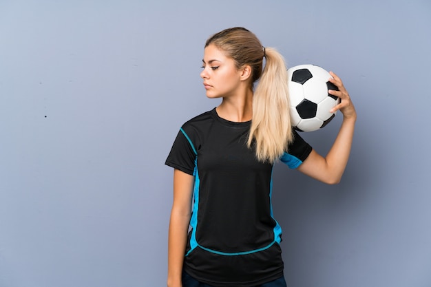 Blonde football player teenager girl over grey wall