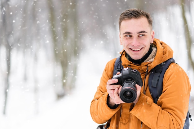 Blonde foto jongen permanent en glimlachend met camera op de winter bos achtergrond