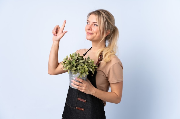 Blonde gardener woman holding a plant over isolated background pointing with the index finger a great idea