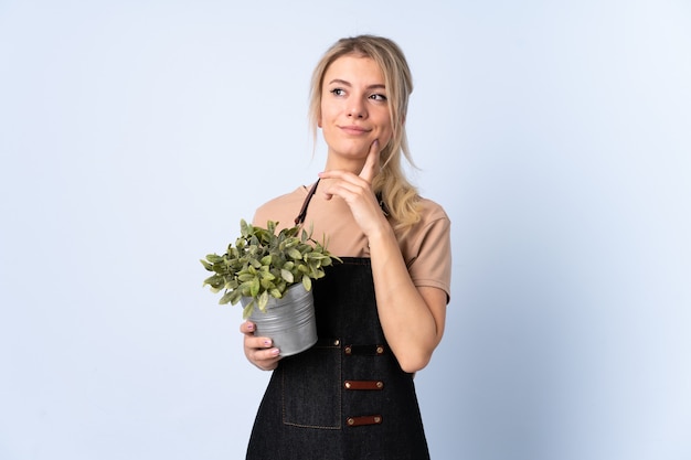 Blonde gardener woman holding a plant over isolated  thinking an idea