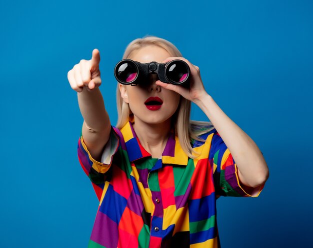 Blonde girl in 90s shirt with binoculars on blue space