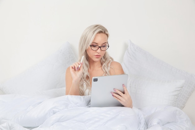 blonde girl in bed with white pillows and a blanket in a bright bedroom, home textiles