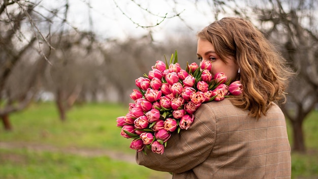 Blonde girl in beige jacket with a large bouquet of pink tulips