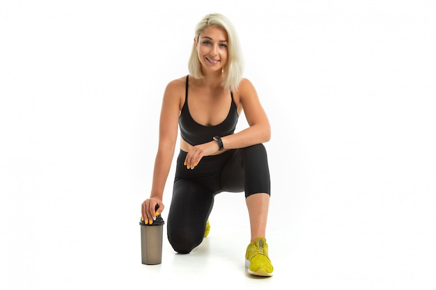 Blonde girl in a black sports uniform kneels isolated white