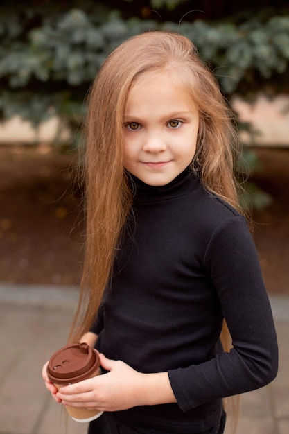 a blonde girl in a black sweatshirt is standing on the street and holding coffee in her hands