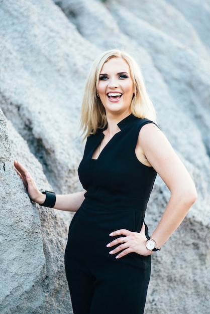 Blonde girl in a black trouser suit with blue eyes on the background of a granite quarry from gray rubble