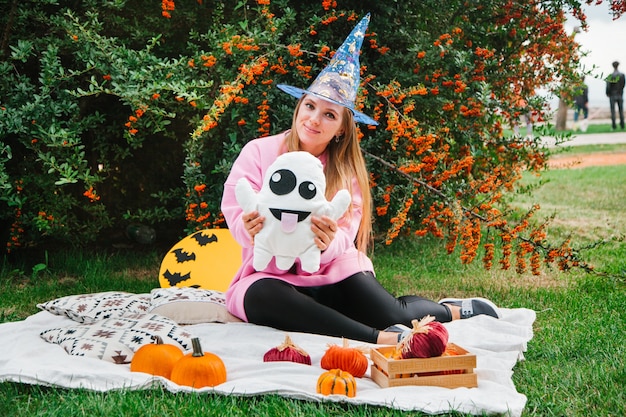 Blonde girl on the blanket in the park on the lawn with a ghost and pumpkins Halloween symbols