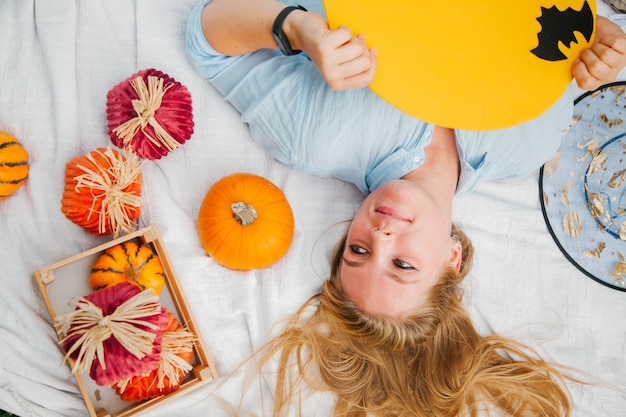 Blonde girl on the blanket in the park on the lawn with a ghost and pumpkins Halloween symbols