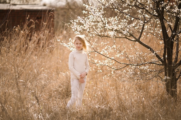 花の咲く庭でブロンドの女の子。白い花と春の背景