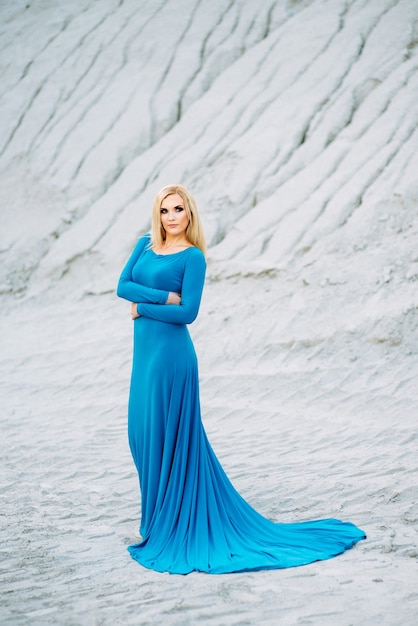 Blonde girl in a blue dress with blue eyes in a granite quarry against the background of gravel