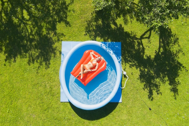 a blonde girl of european appearance sunbathes on an air mattress in a small outdoor pool on a summe