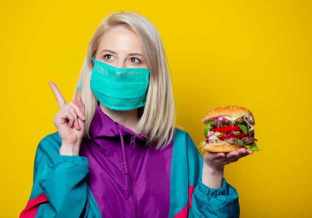 Blonde girl in face mask with burger