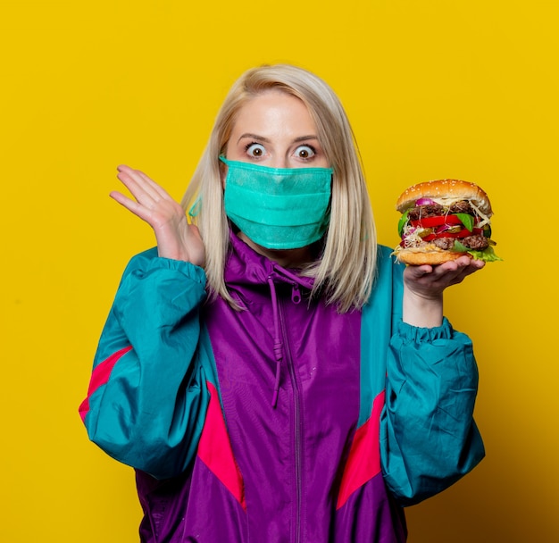 Blonde girl in face mask with burger