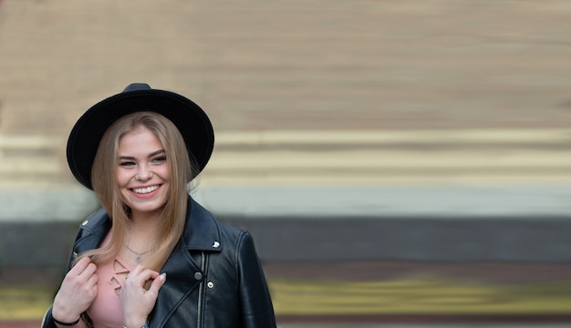 Ragazza bionda in cappello e ruota panoramica nella città moderna