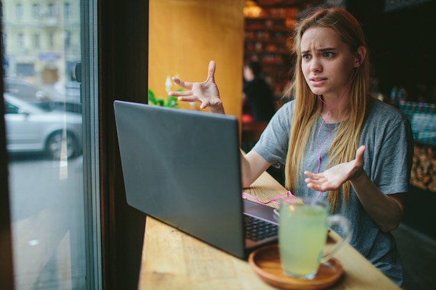 Ragazza bionda che ha una videochiamata sul portatile al bar