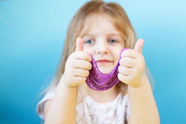 Blonde girl hold purple slime isolated on a blue background child playing with a slime toy