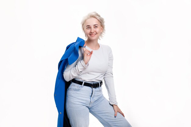 Blonde girl holding a blue coat in her hand smiles broadly on a white background