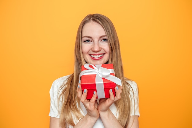 blonde girl holding a gift box isolated over yellow background in studio