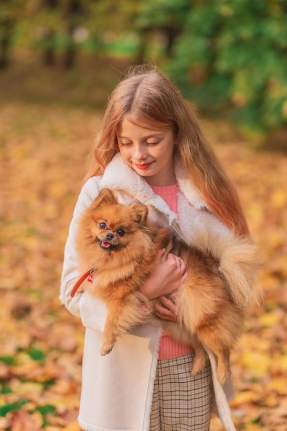 A blonde girl holding a spitz in her arms in the park.