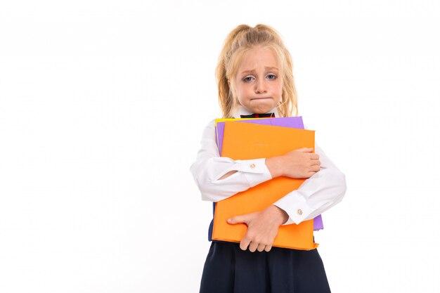 Blonde girl holds books against a white wall