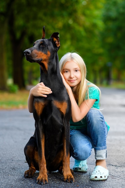 Blonde girl hugs her beloved dog in summer park.