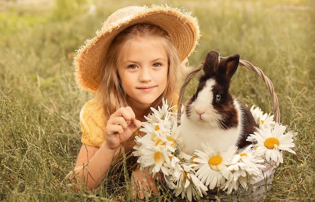 Блондинка в соломенной шляпе лежит на траве рядом с кроликом, сидящим в корзине с ромашками