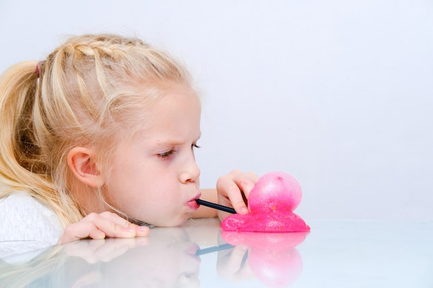 Blonde girl inflating bubble from pink glitter slime