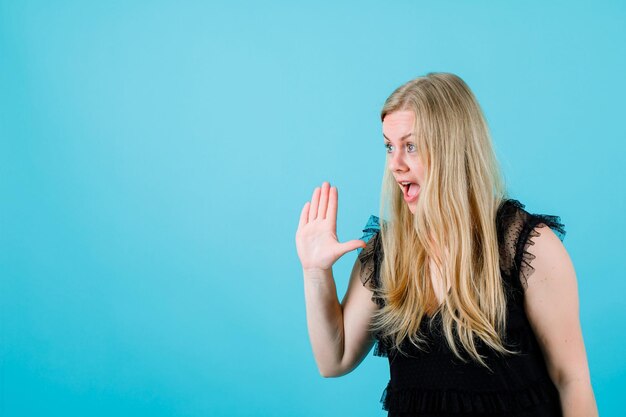 Blonde girl is screaming by raising up her handful on blue background