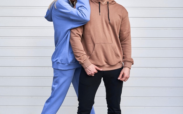 Blonde girl is standing in blue sport outfit Man wears brown hoodie and black pants Couple is wearing street matching outfit