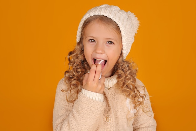 ニットジャケットと冬のニット帽をかぶったブロンドの女の子が彼女の口に風邪薬を注ぐ