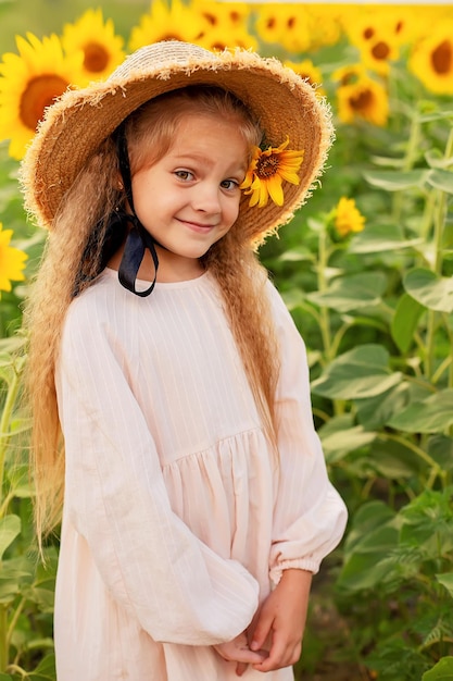 a blonde girl in a linen dress in a straw hat stands in a sunflower field