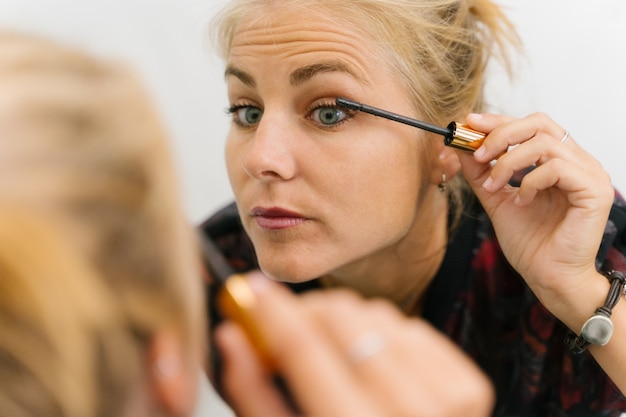 Blonde girl making up herself in mascara