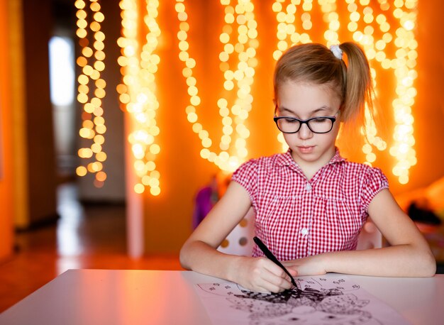 Blonde girl in the pink dress and big black glasses drawing santa claus