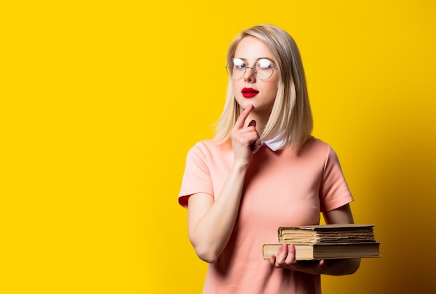 Blonde girl in pink dress and glasses with books on yellow background