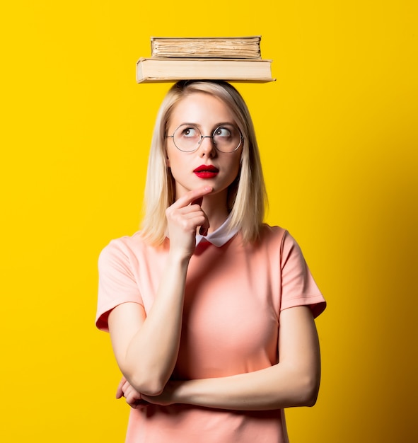 Blonde girl in pink dress and glasses with books on yellow space