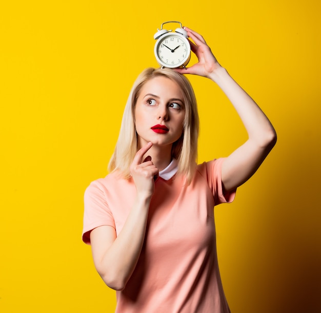 Blonde girl in pink dress with alarm clock on yellow space