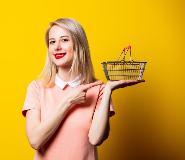 Blonde girl in pink dress with shopping basket on yellow space